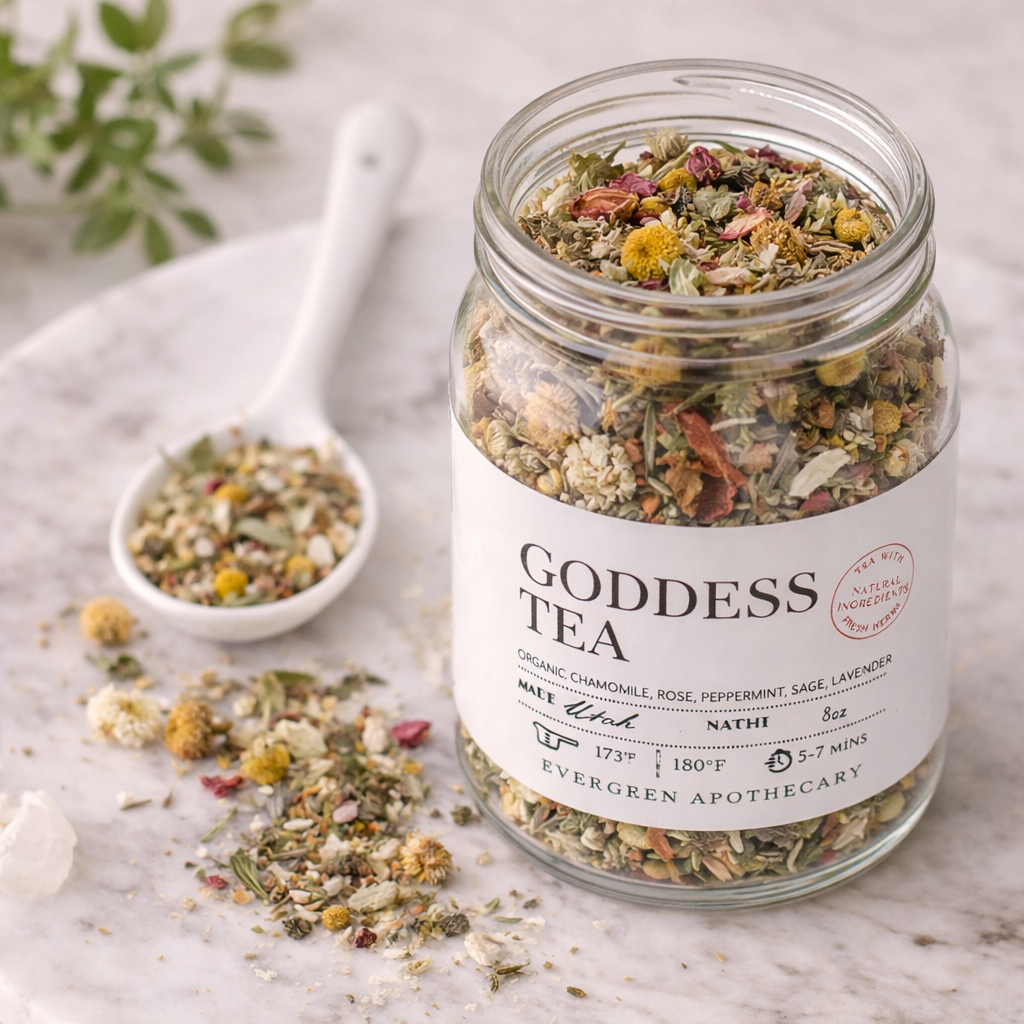 Open jar of Goddess Tea herbal blend on a marble surface with a spoon of loose tea, scattered botanicals, and a soft neutral background